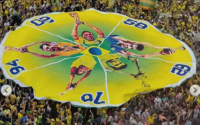 ista aérea de uma multidão em um estádio de futebol, onde torcedores uniformizados em verde e amarelo formam um padrão denso de cores, simbolizando a união coletiva durante uma partida de Copa do Mundo.